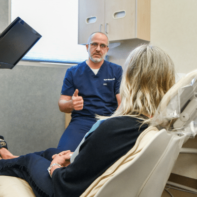 Veneers vs crowns: which is right for you? 2 A man in blue uniform talking to a woman in a dental chair, representing veneers vs crowns